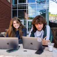 Two students outside working on laptops