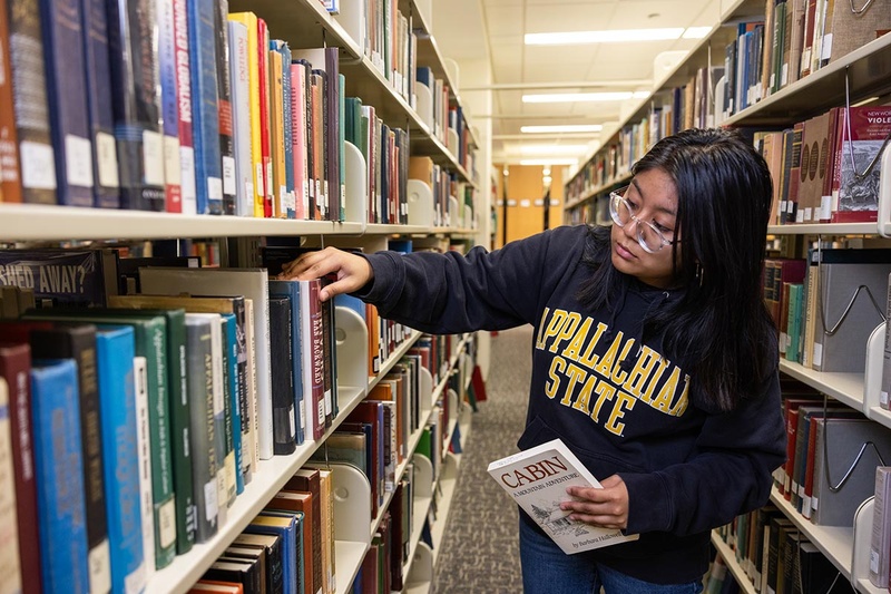 Student removing book from Library shelf